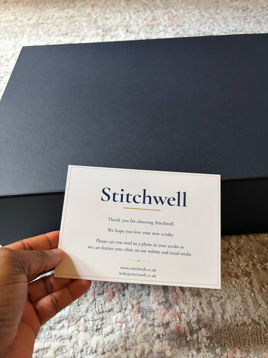 A hand holding a Stitchwell thank-you card in front of a packaged uniform order