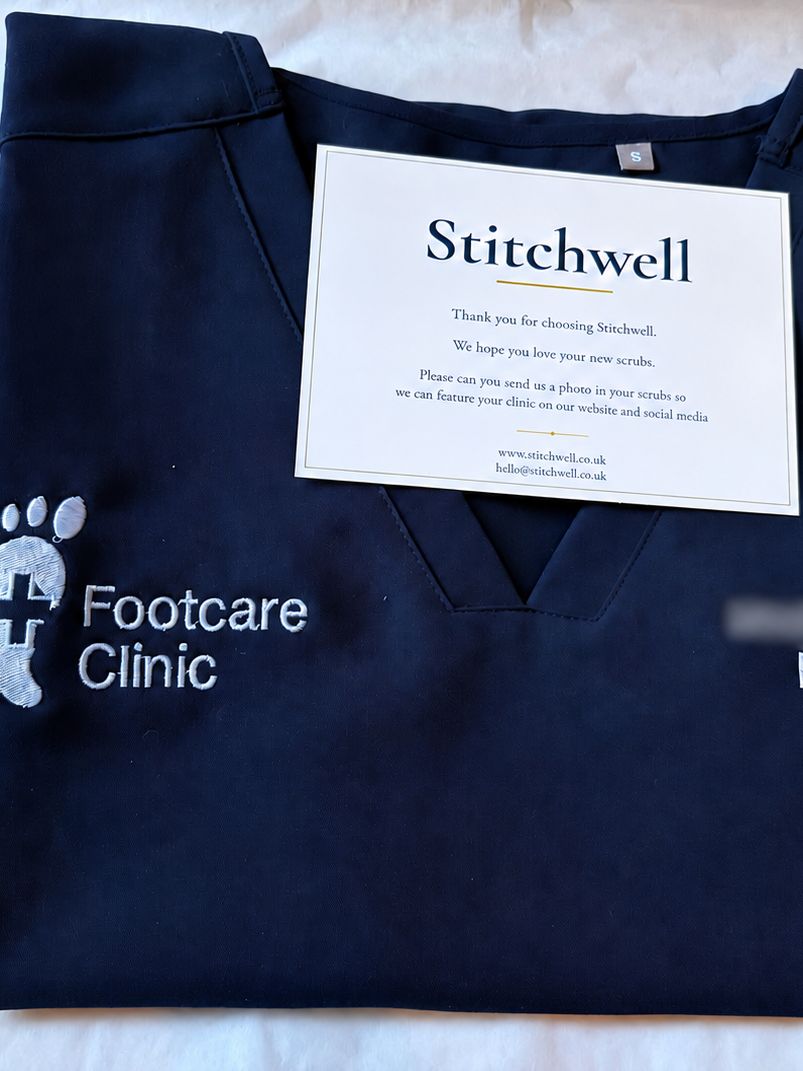 Folded personalised scrub top embroidered with a clinic logo and role, packaged with a Stitchwell thank-you card